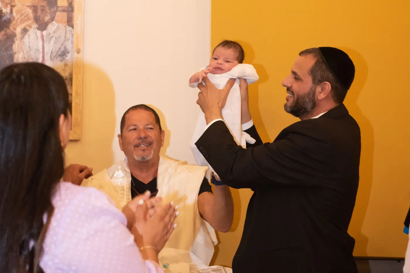 הסנדק מרים בעדינות את התינוק בטקס הברית