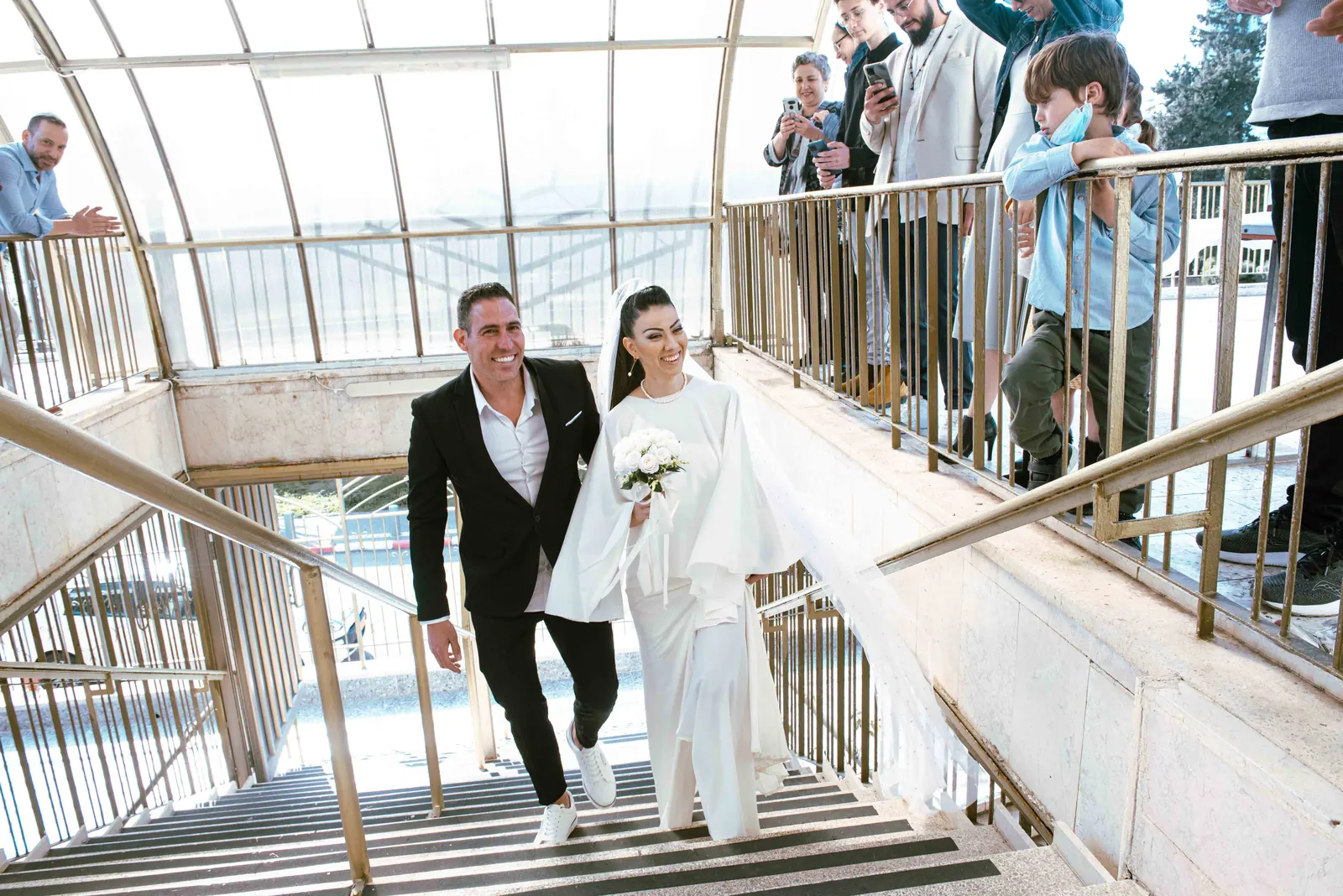 חתן וכלה יורדים במדרגות כשהאורחים צופים ומצלמים